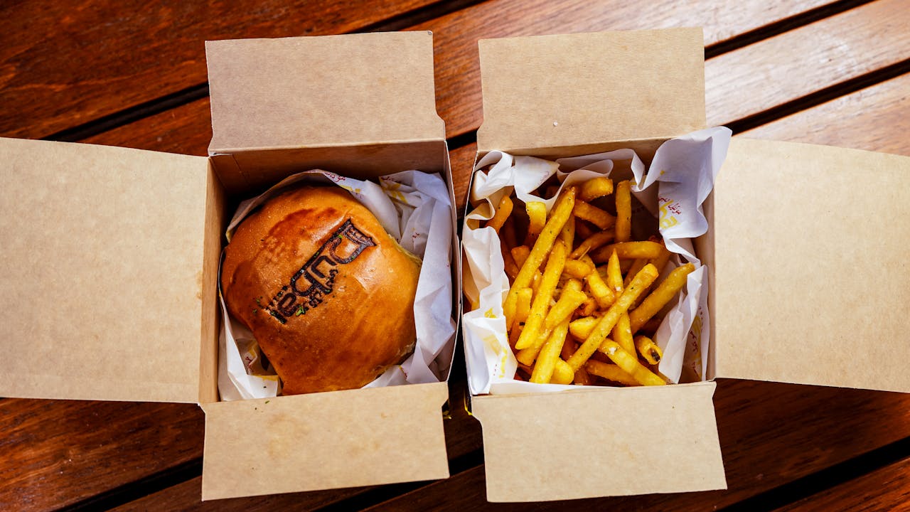 services-04 Overhead view of a burger and fries in eco-friendly paper boxes on a wooden table.
