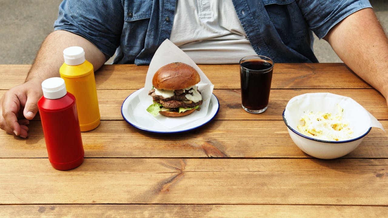 services-03 Casual dining with a burger, soda, and sauces at outdoor table. Perfect for summer vibes.